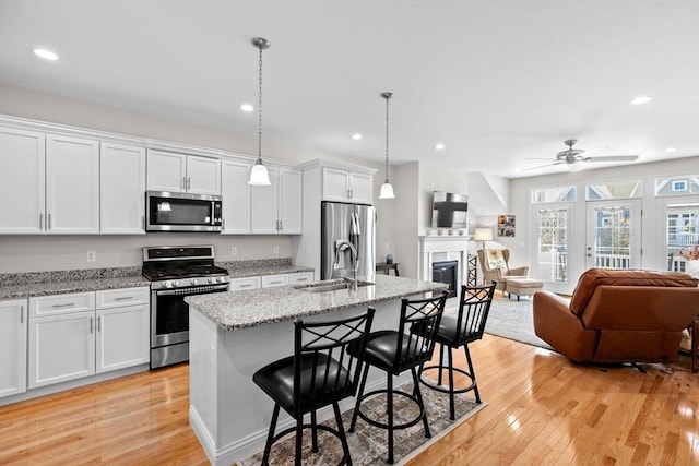 kitchen with a glass covered fireplace, light wood-style floors, open floor plan, a sink, and stainless steel appliances