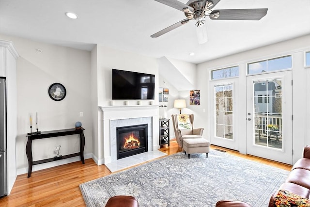 living area with a ceiling fan, baseboards, light wood finished floors, a glass covered fireplace, and recessed lighting