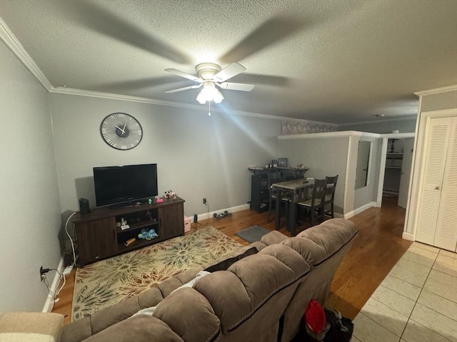 living area featuring a textured ceiling, a ceiling fan, baseboards, ornamental molding, and tile patterned floors