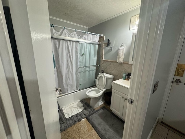 bathroom with bath / shower combo with glass door, wainscoting, a textured ceiling, vanity, and tile walls