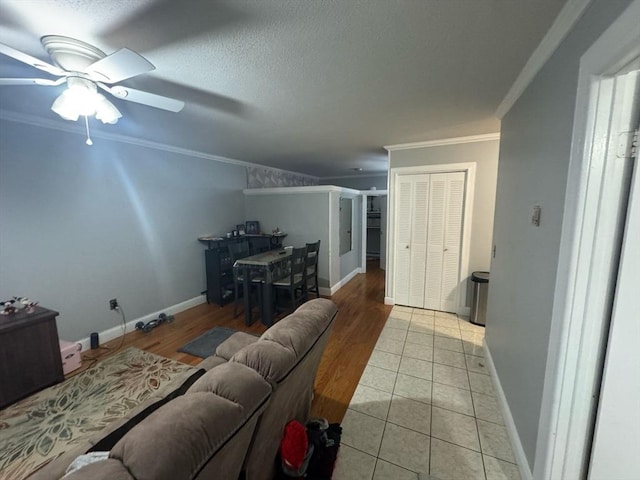 living room with a textured ceiling, ceiling fan, light tile patterned flooring, baseboards, and ornamental molding