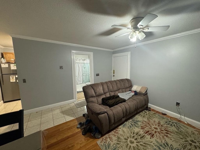 living area featuring light tile patterned floors, baseboards, ceiling fan, ornamental molding, and a textured ceiling