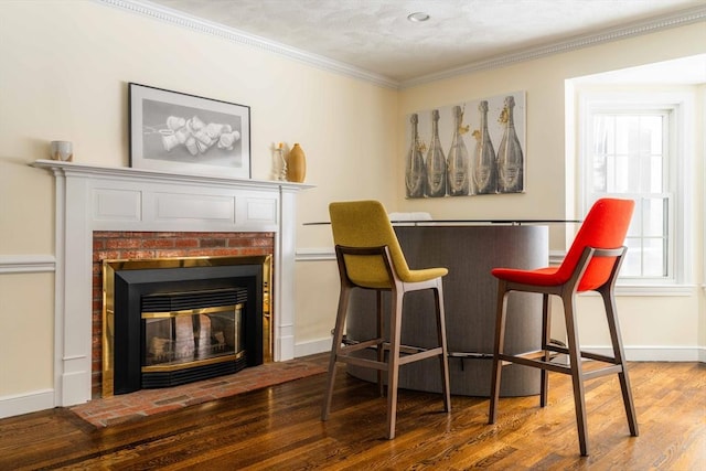 living area with a brick fireplace, baseboards, crown molding, and wood finished floors