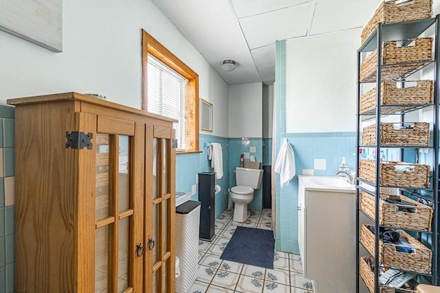bathroom featuring toilet, wainscoting, vanity, and tile walls