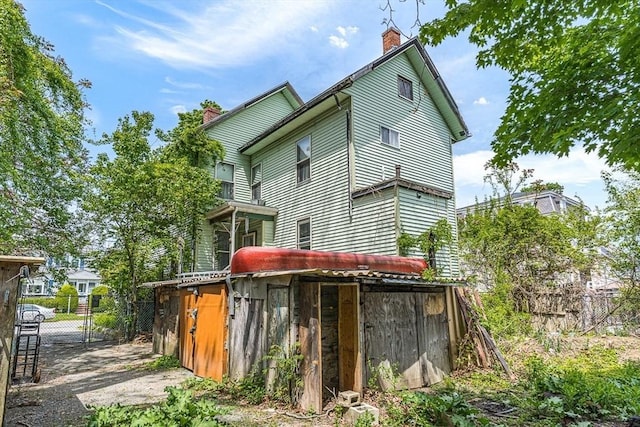 back of house featuring a chimney, fence, and a gate