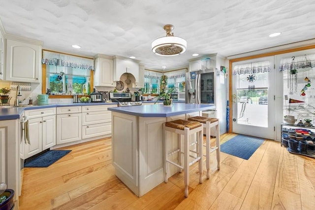 67 Main St, Atkinson, NH 03811 - kitchen with light wood finished floors, dark countertops, a kitchen island, a kitchen bar, and stainless steel refrigerator with ice dispenser