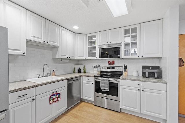 kitchen with sink, white cabinets, light wood-type flooring, decorative backsplash, and stainless steel appliances