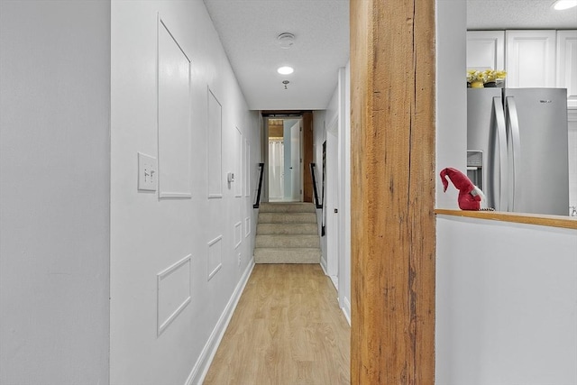 corridor with a textured ceiling and light hardwood / wood-style flooring