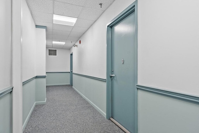 hall with a paneled ceiling and light carpet