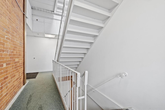 stairway featuring brick wall and carpet flooring