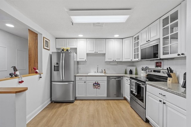 kitchen with light hardwood / wood-style floors, appliances with stainless steel finishes, white cabinets, sink, and backsplash