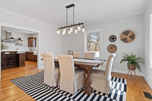 dining space featuring light wood finished floors, visible vents, baseboards, and ornamental molding