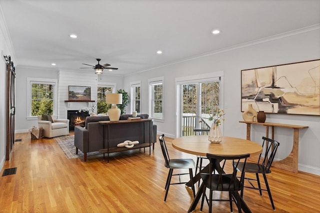 dining space featuring visible vents, crown molding, a barn door, light wood-type flooring, and a large fireplace