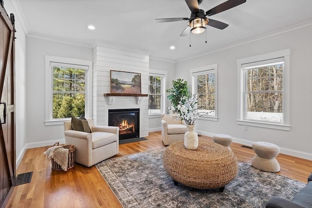 living area with a barn door, light wood-style flooring, and ornamental molding