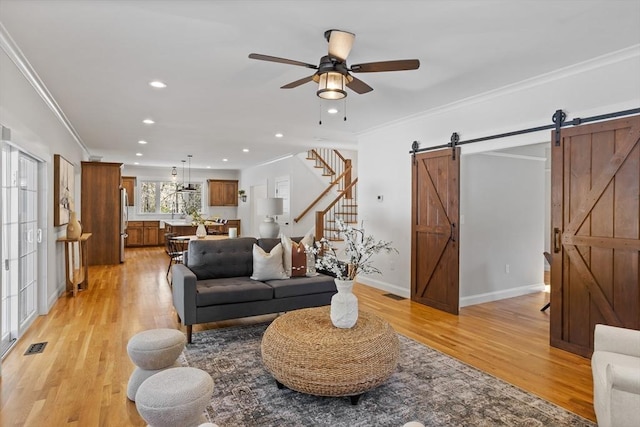 living area featuring a barn door, crown molding, visible vents, and light wood finished floors