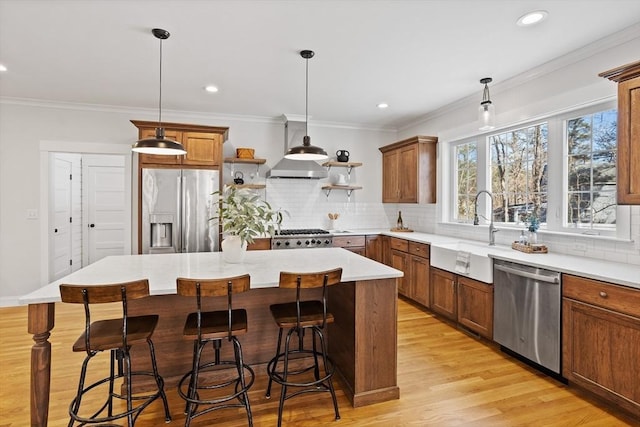 kitchen with brown cabinetry, a sink, stainless steel appliances, light wood-style floors, and crown molding