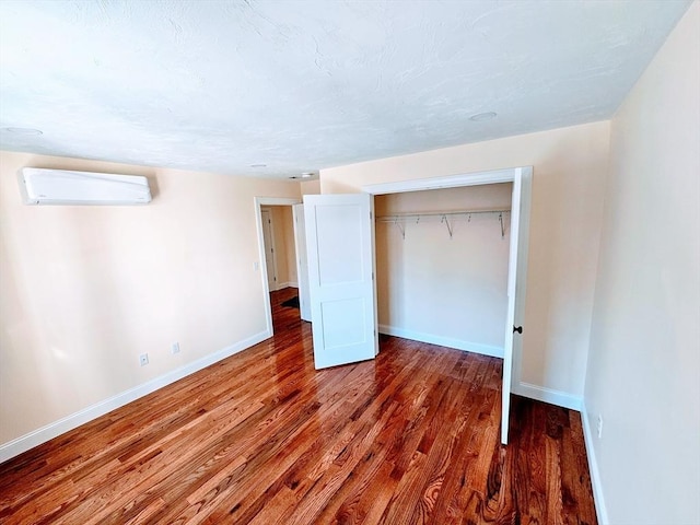 unfurnished bedroom with a closet, an AC wall unit, baseboards, and wood finished floors