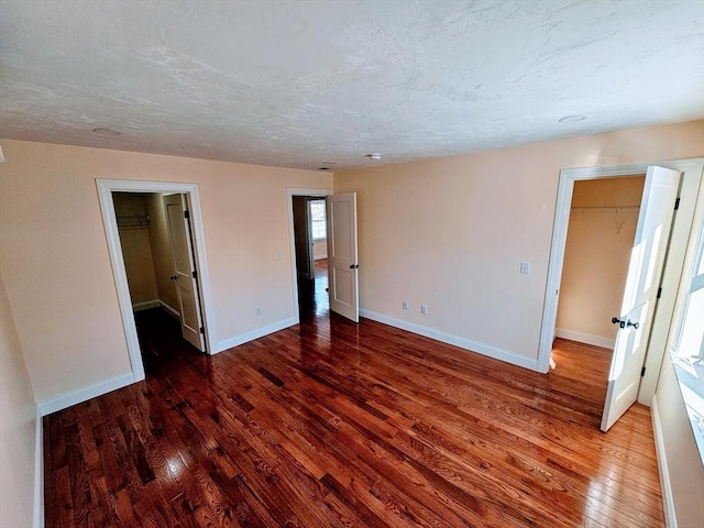 unfurnished bedroom featuring a walk in closet, wood-type flooring, a textured ceiling, and baseboards