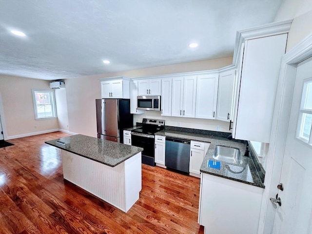 kitchen with appliances with stainless steel finishes, a center island, white cabinets, and wood finished floors