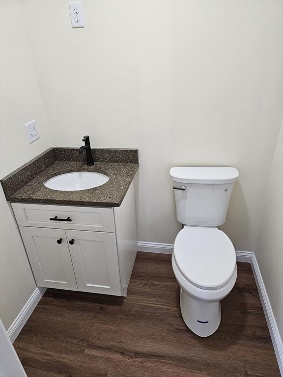 half bath with toilet, baseboards, wood finished floors, and vanity