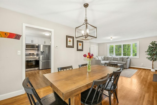 dining room with a chandelier, baseboards, light wood-type flooring, and a baseboard heating unit