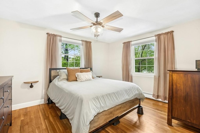 bedroom featuring a ceiling fan, light wood-type flooring, baseboards, and a baseboard radiator