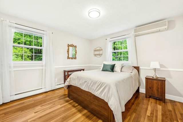 bedroom featuring an AC wall unit, baseboards, and wood finished floors