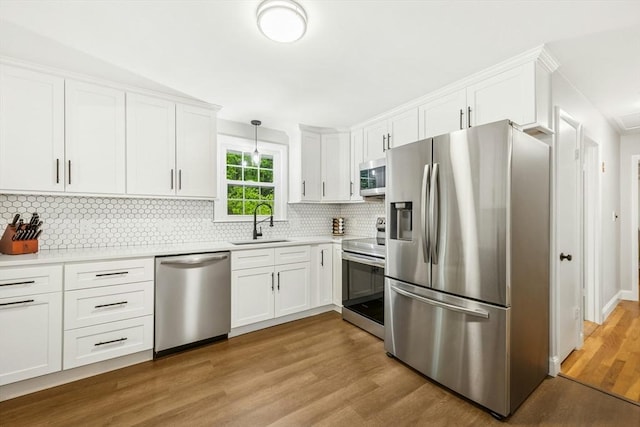 kitchen with stainless steel appliances, a sink, wood finished floors, light countertops, and white cabinets