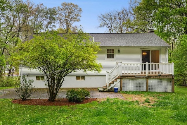 back of property with a lawn, a chimney, a wooden deck, and a shingled roof