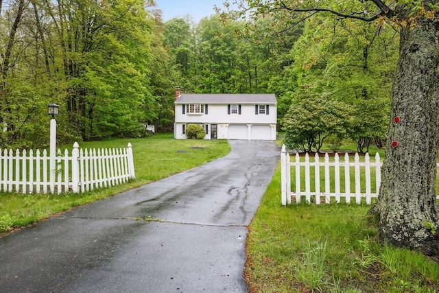 view of front of property featuring a chimney, a forest view, fence, a front yard, and aphalt driveway