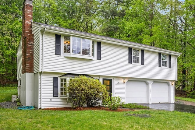 colonial home with a chimney, an attached garage, asphalt driveway, a front yard, and view of wooded area