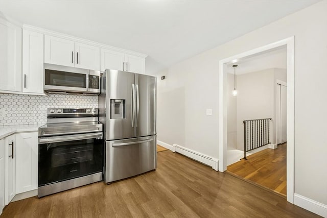 kitchen featuring baseboard heating, light wood-style flooring, backsplash, light countertops, and appliances with stainless steel finishes