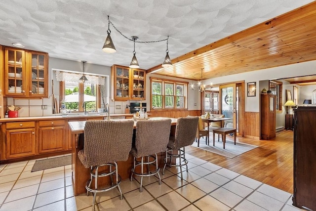 5 Vasa St, Billerica, MA 01862 - kitchen with an island with sink, brown cabinetry, healthy amount of natural light, light tile patterned floors, and a wainscoted wall