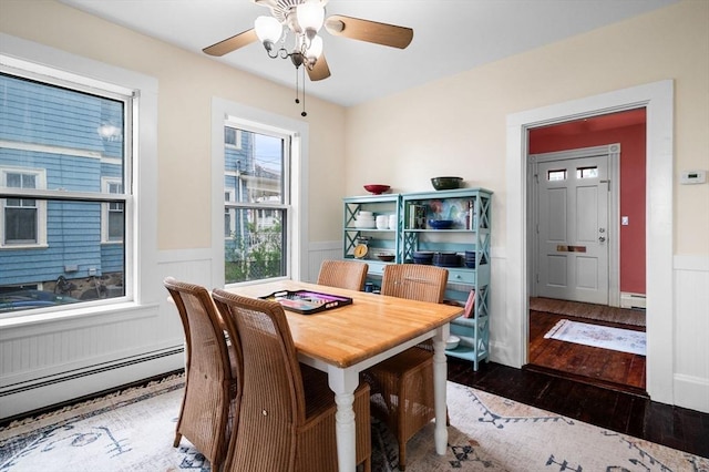 dining area featuring wood-type flooring, wainscoting, a baseboard radiator, a ceiling fan, and a baseboard heating unit