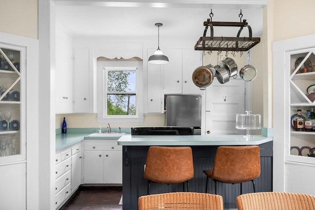 kitchen with a sink, white cabinetry, light countertops, fridge, and a kitchen breakfast bar