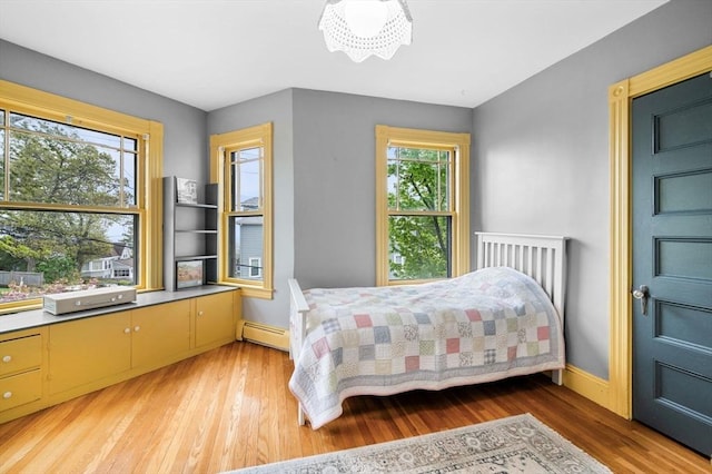bedroom featuring light wood finished floors, baseboards, and a baseboard radiator