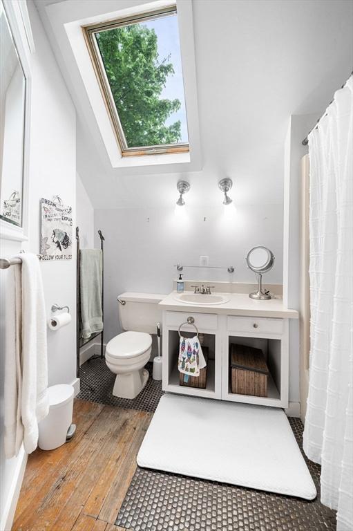 bathroom with hardwood / wood-style flooring, toilet, a sink, a skylight, and a shower with curtain