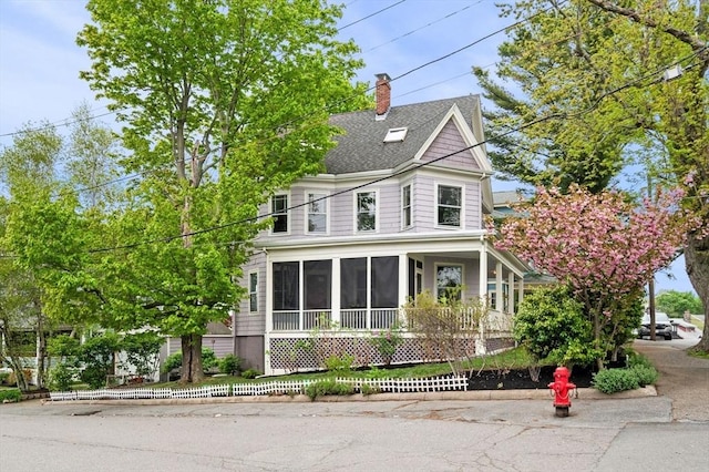 view of front facade with a sunroom, a chimney, and roof with shingles