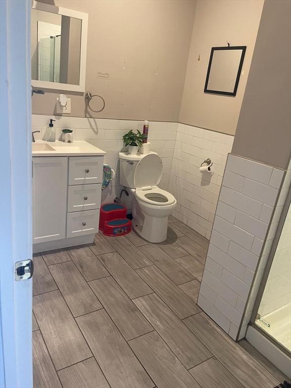 108 Grove St, Lynn, MA 01905 - full bathroom featuring tile walls, vanity, a wainscoted wall, wood tiled floors, and a shower with shower door