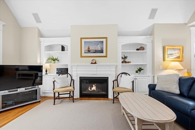 living room with lofted ceiling, light wood-style flooring, a glass covered fireplace, visible vents, and built in features