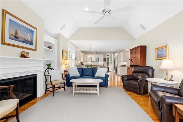 living area featuring a ceiling fan, a glass covered fireplace, built in features, vaulted ceiling, and light wood-style floors