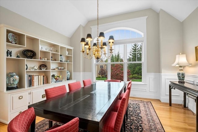 dining area with lofted ceiling, a wainscoted wall, a chandelier, and light wood-style flooring