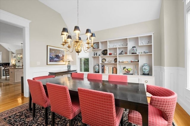 dining space with wainscoting, lofted ceiling, a notable chandelier, and wood finished floors