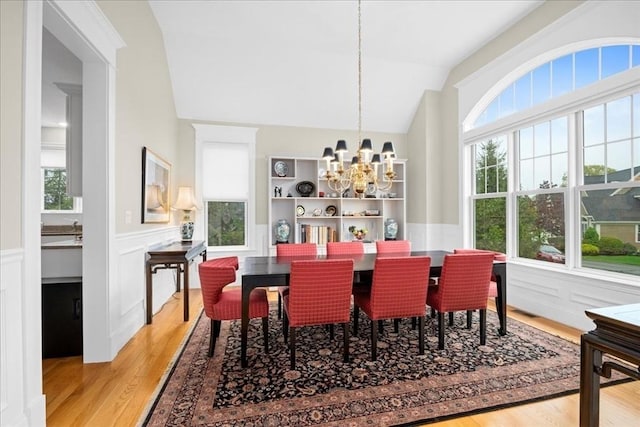 dining space with light wood finished floors, an inviting chandelier, a wainscoted wall, a decorative wall, and lofted ceiling
