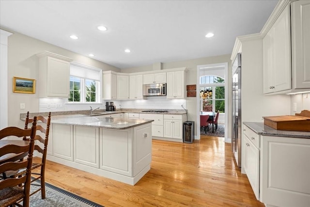 kitchen featuring a sink, light wood-type flooring, stainless steel microwave, decorative backsplash, and recessed lighting