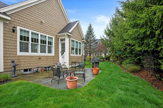back of property with a patio area, roof with shingles, and a lawn