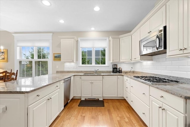 kitchen featuring a sink, a peninsula, stainless steel appliances, white cabinets, and light wood-type flooring