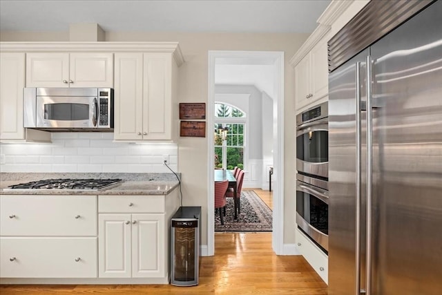 kitchen with light wood finished floors, white cabinets, appliances with stainless steel finishes, decorative backsplash, and light stone counters