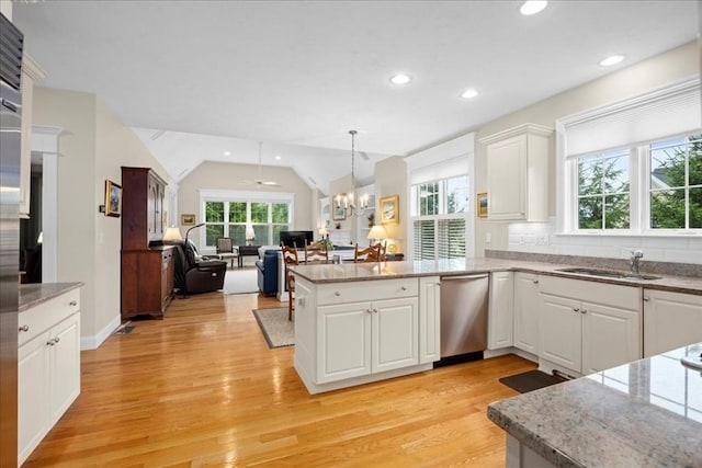 kitchen with a peninsula, a sink, open floor plan, stainless steel dishwasher, and light wood-style floors