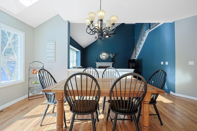 dining space featuring vaulted ceiling, light wood-type flooring, a notable chandelier, and baseboards